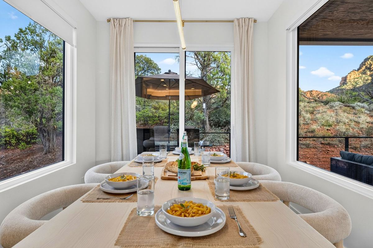Dining table set for a meal beside corner windows.