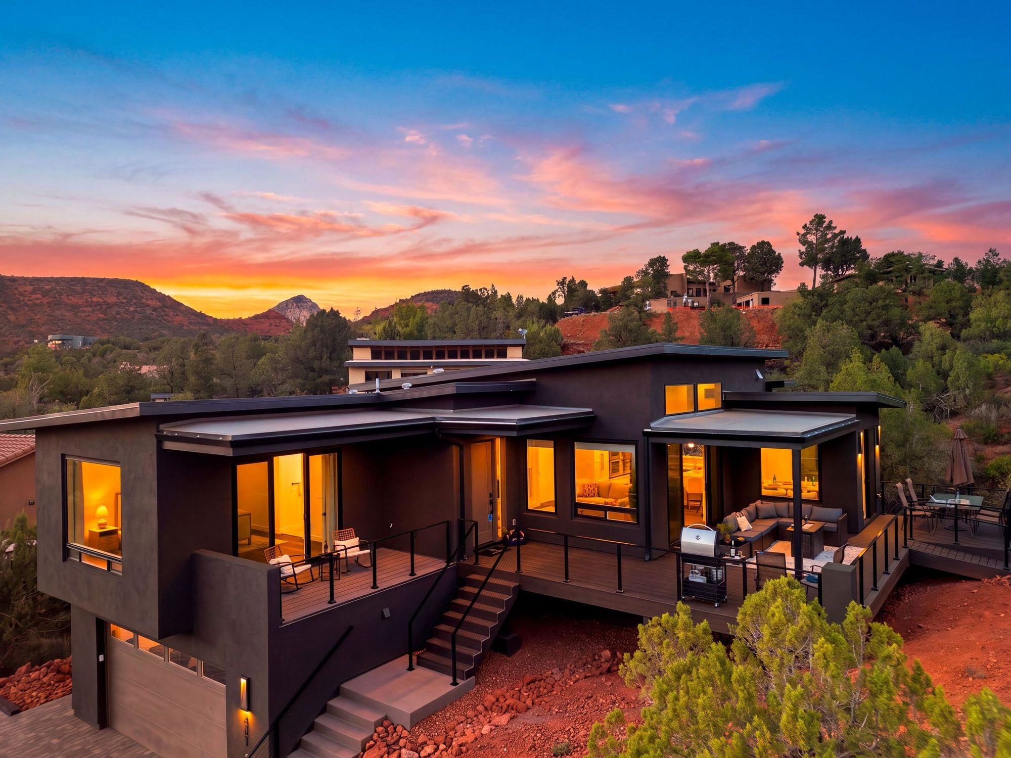 Casa Alta at sunset: a low, dark modern house with lit windows on a hillside of red earth and juniper.