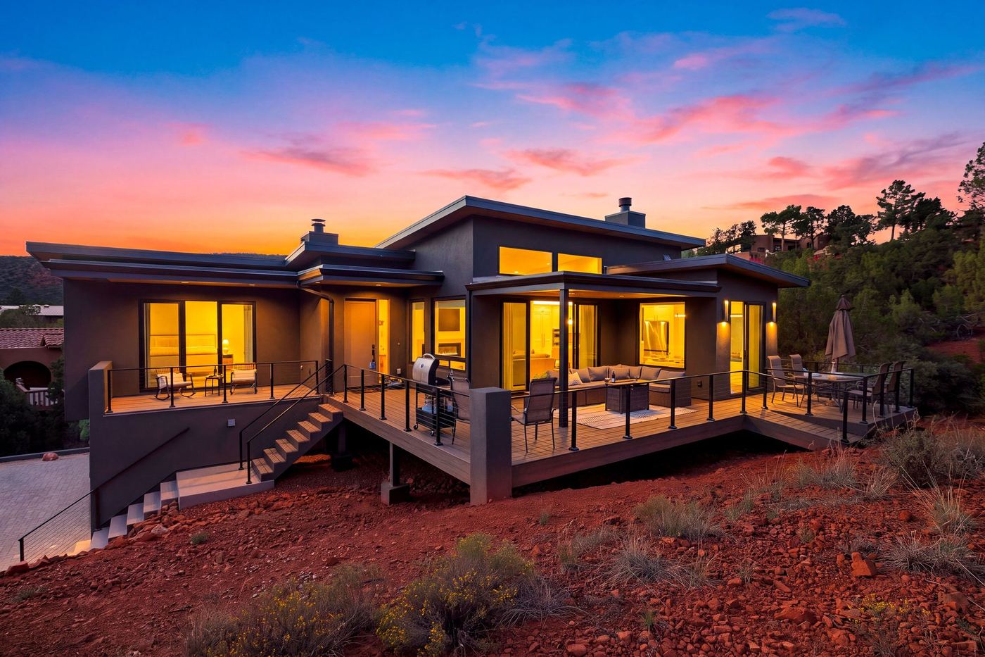 The house and its wraparound deck at sunset, windows glowing under a pink and orange sky.
